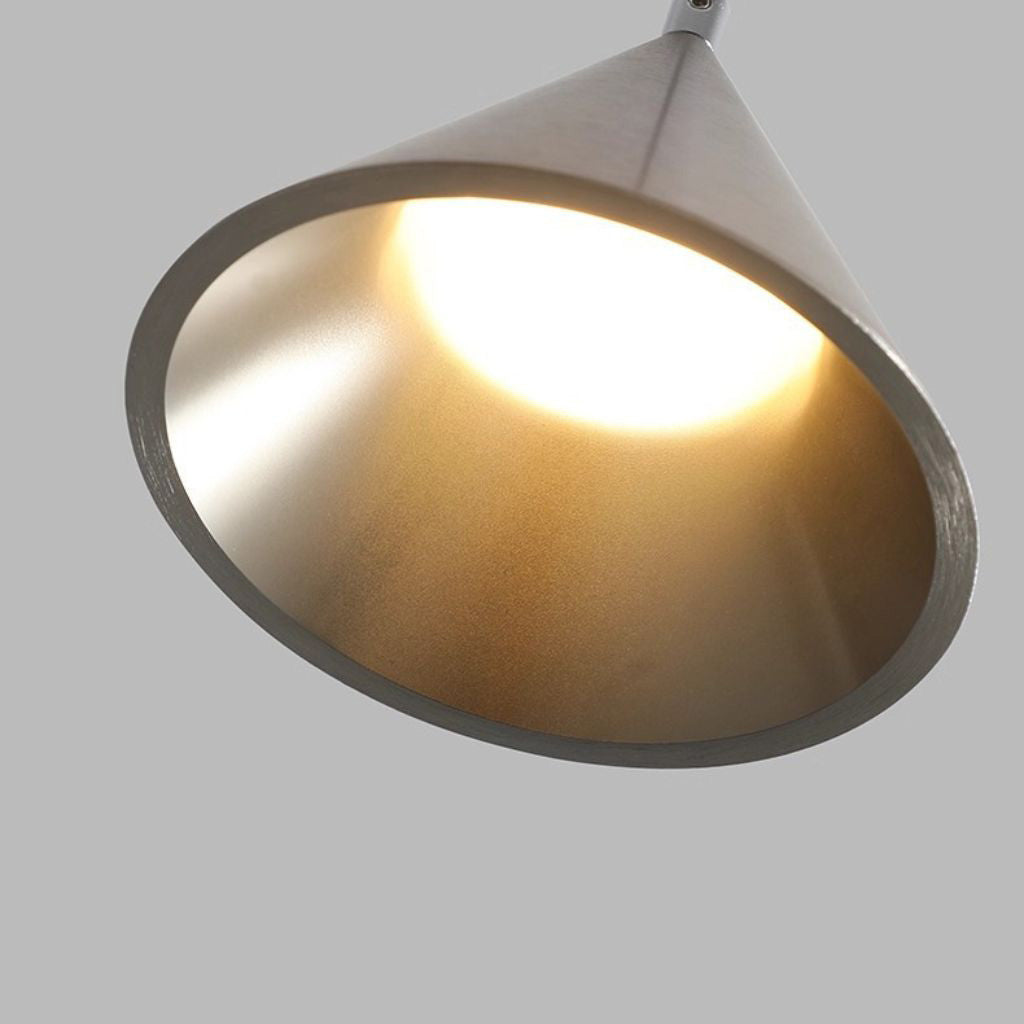 A modern cone-shaped pendant light with a brushed silver metal exterior and a warm glowing yellow interior, shown against a solid gray background.