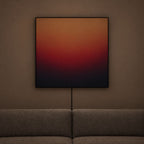 A square abstract wall art print with a gradient from warm orange and red to deep red and black, hanging on a brown wall above a gray sofa.
